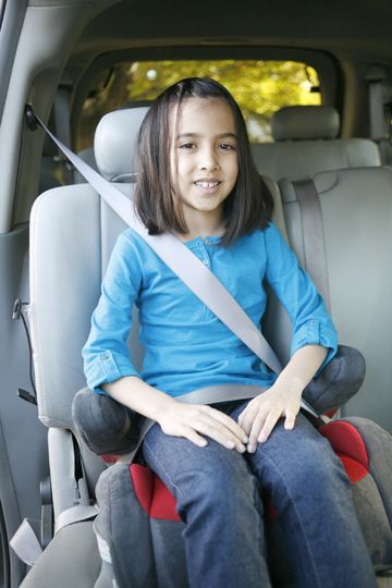 A girl uses a booster seat in a vehicle. 